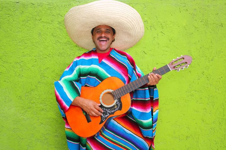 メキシコの伝統的な帽子とポンチョ姿の男性がギターを弾いているイメージ