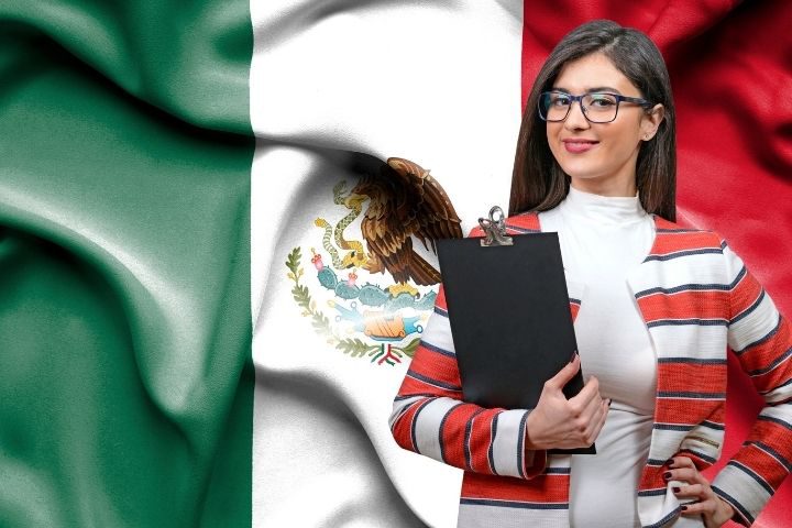 メキシコの国旗を背景に右側に立つメガネの女性の画像