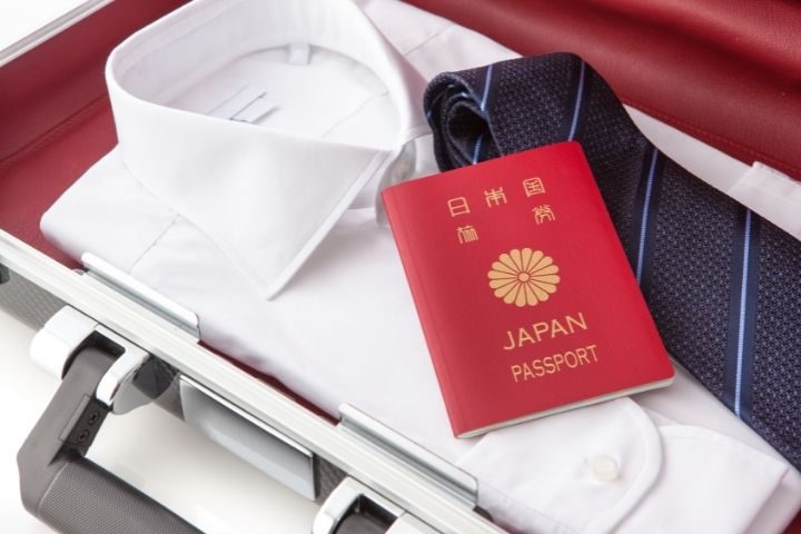 スーツケースの中に白いワイシャツと紺のネクタイとパスポートが入っているイメージ画像