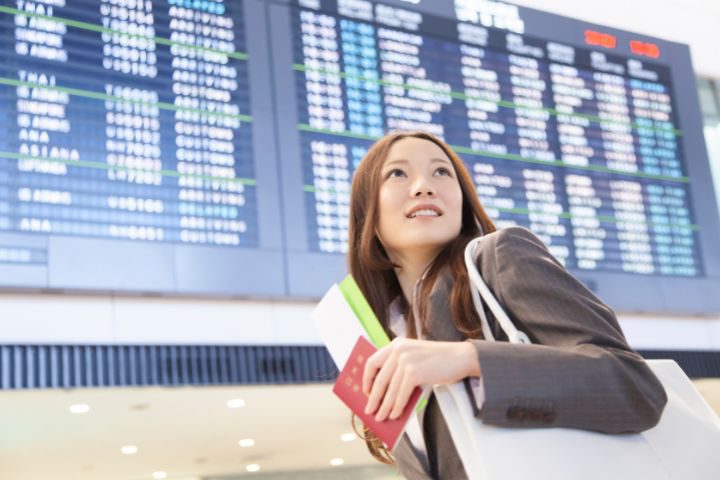 パスポートを手に空港を歩く女性の画像