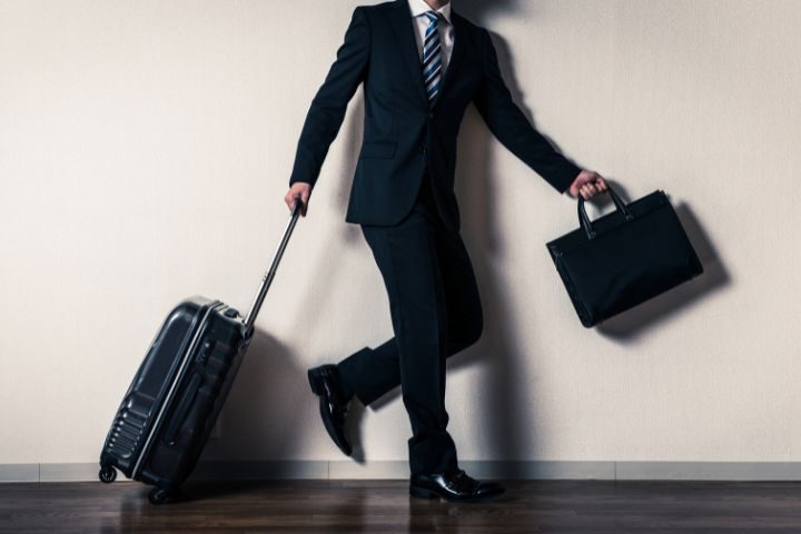 カバンとスーツケースを持って出かけようとしているビジネスマンのイメージ