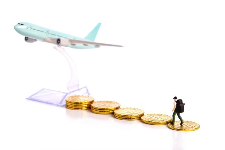 飛行機のミニチュアに向かって積み上げられているコインを登ろうとしている人形のイメージ