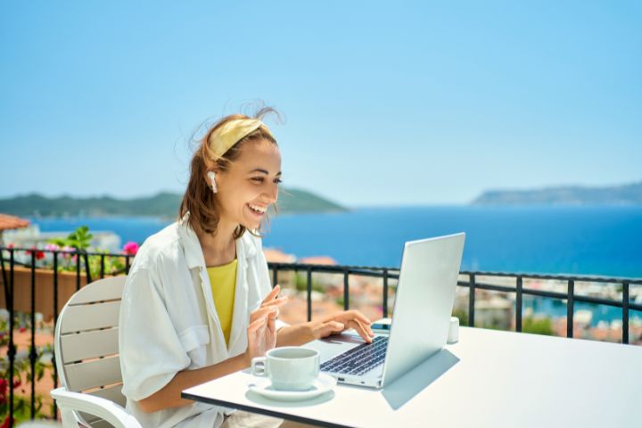 海が見えるテラス席でパソコンで会話しながら仕事している女性の画像