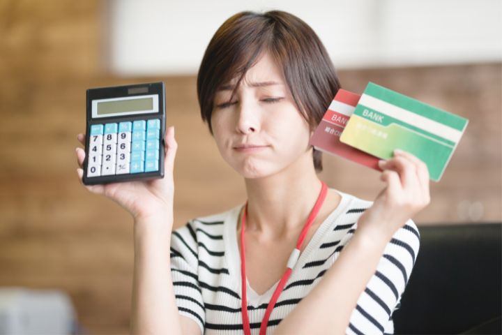 通帳と電卓を手に悩んでいる様子の女性