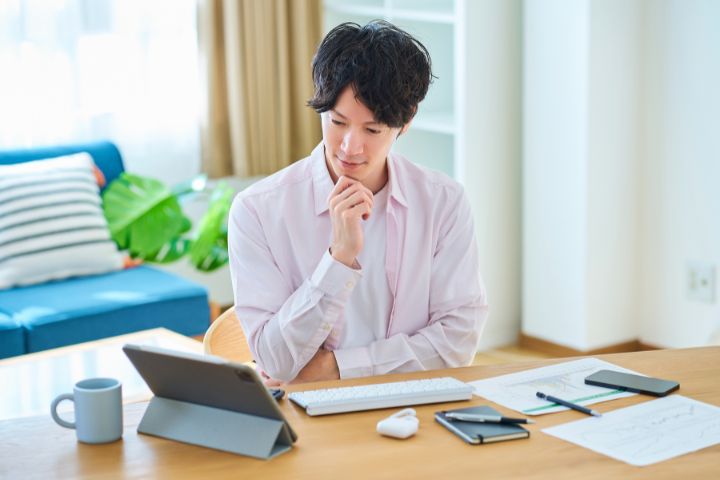 タブレットの画面を見ながら考え事をする男性のイメージ