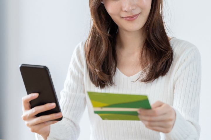 通帳とスマホを眺めている女性のイメージ